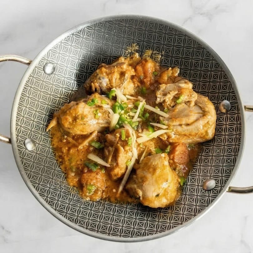 Chicken karahi in a decorative metal serving dish, garnished with ginger and green chilies.