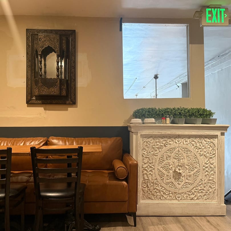 Restaurant interior with a brown leather booth, wooden tables, and an intricately carved white cabinet.